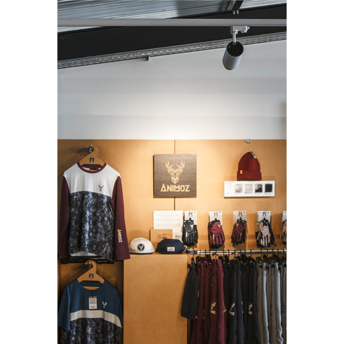 Black track lighting fixture, mounted on ceiling, illuminating Animoz apparel display.