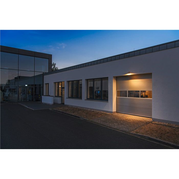 Gray steel sectional garage door with windows on a white building.