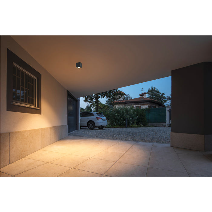 Modern gray cube ceiling light illuminating a covered driveway.