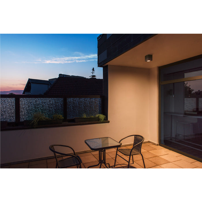 Modern outdoor patio with black wicker chairs, glass table, and flush-mounted gray ceiling light.