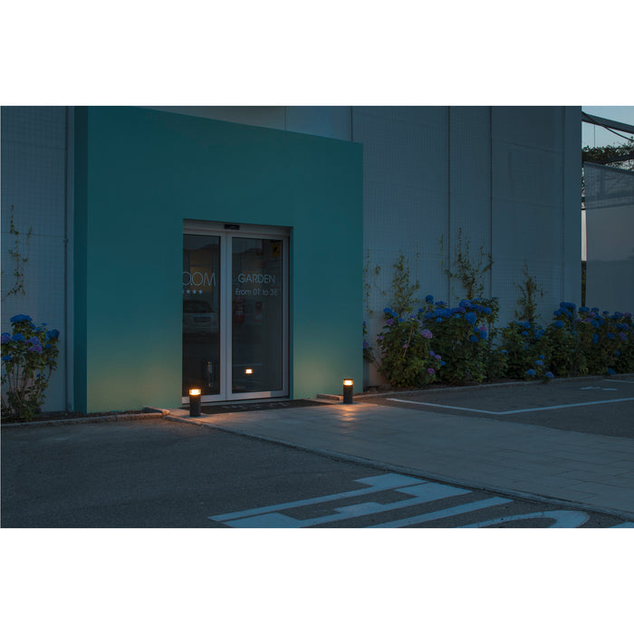 Black bollard lights illuminating a building entrance at dusk.