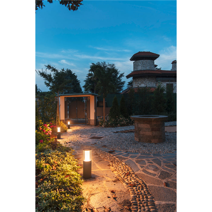Black metal outdoor path light with warm light, ground mounted.