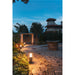 Black metal outdoor path light with warm light, ground mounted.