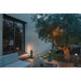 Gray metal bollard lights illuminating a modern patio with wood decking and an olive tree.
