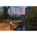 Black bollard lights on a wood deck overlooking a pond and building.
