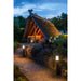 Black bollard lights illuminating a brick path leading to a thatched-roof gazebo in a garden setting.