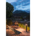 Dark bronze bollard light, ground-mounted, illuminating a park bench and pond at dusk.