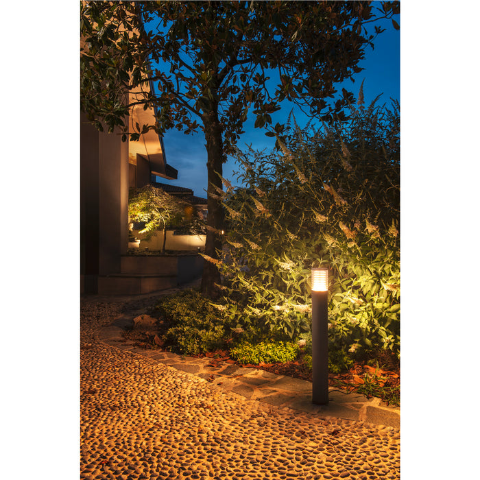 Dark gray bollard light illuminating a pebble stone path and garden at night.