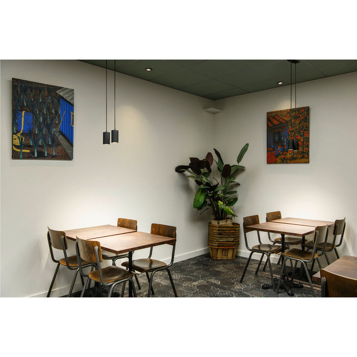 Restaurant interior with wood tables, metal chairs, black pendant lights, and colorful paintings.