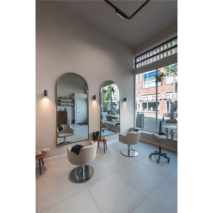 Salon interior with two arched gold-framed mirrors, beige chairs with chrome bases, and large window.