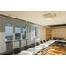 Modern conference room with a long white table, black chairs, glass walls, and wood floor.