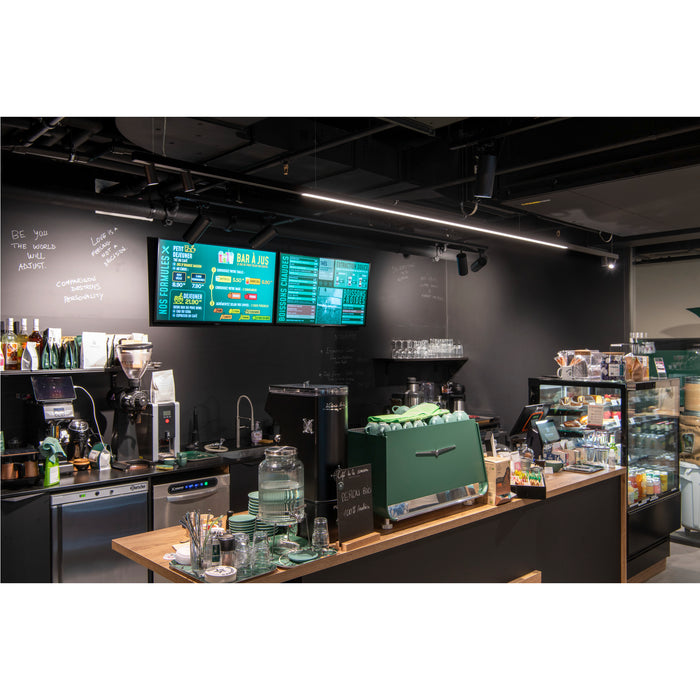Coffee shop interior with a green espresso machine, wood countertop, and digital menu board.