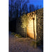 Gabion wall with wood panels, filled with rocks, next to a small tree illuminated by a ground spotlight.