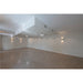 Empty room with recessed and wall-mounted black metal sconce lighting, white walls and ceiling, and speckled brown flooring.