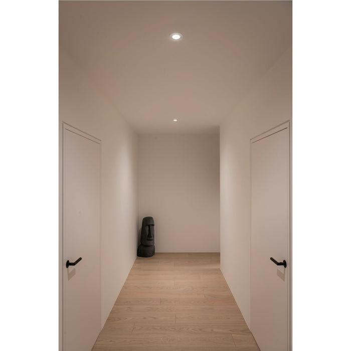 Hallway with light wood floors, white walls and doors, recessed lighting, and a dark stone Moai statue.