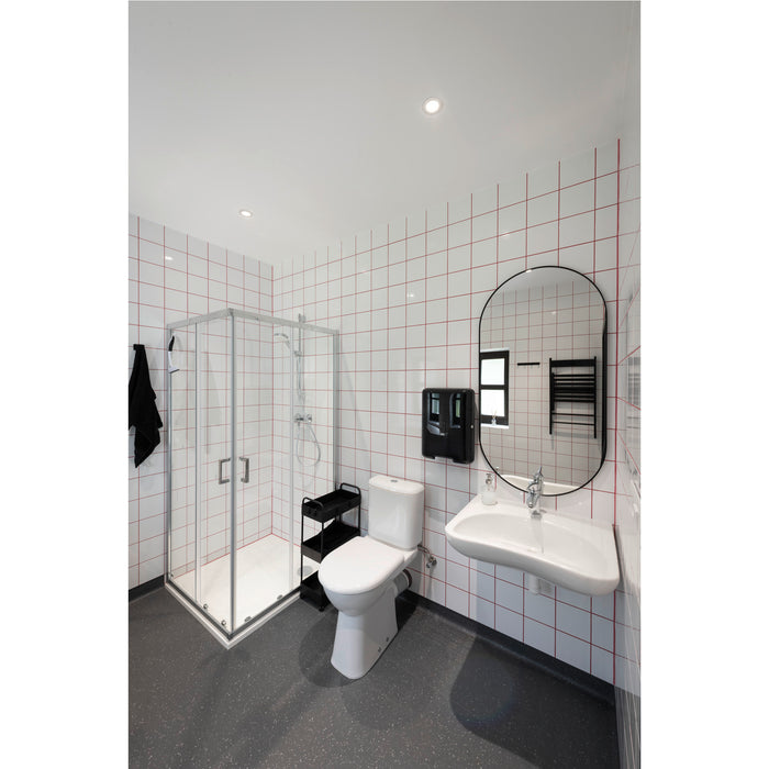Modern bathroom with white tile, red grout, wall-mounted sink, oval mirror, glass shower, and gray speckled flooring.