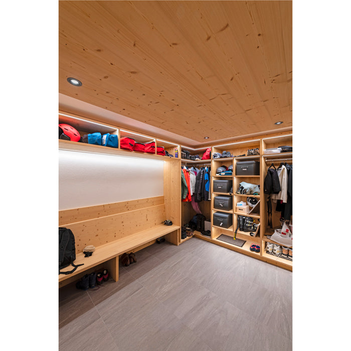 Wood closet with built-in bench, shelves, and hanging space for ski gear and clothing, with gray tile flooring.