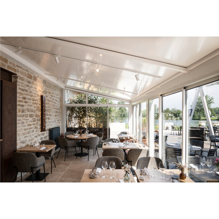 Restaurant interior with wood tables, gray upholstered chairs, stone wall, and white track lighting.