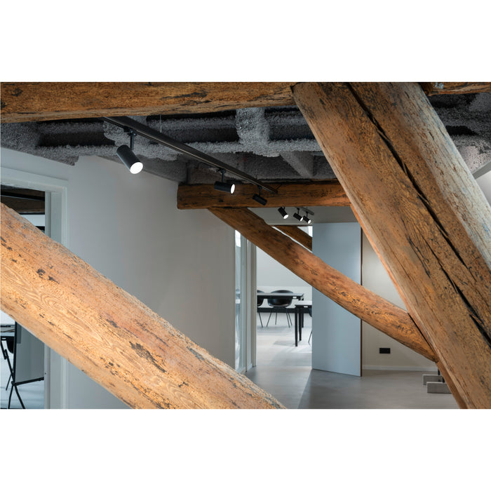 Black track lighting with cylindrical heads, surface mounted on a wood beam ceiling.
