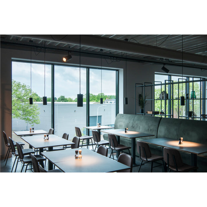 Restaurant interior with metal chairs, dark tables, green banquette seating, and black pendant lights.