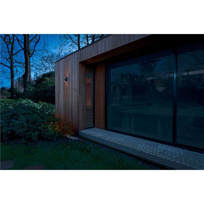 Black wall-mounted outdoor light fixture on wood siding of modern building.