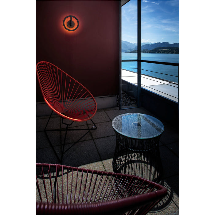 Outdoor patio with red string chairs, glass-top table, and round black wall-mounted light fixture.