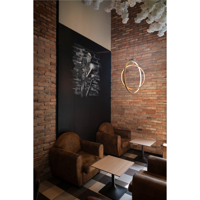 Interior with brown leather armchairs, wood tables, brick wall, and gold metal ring pendant light.