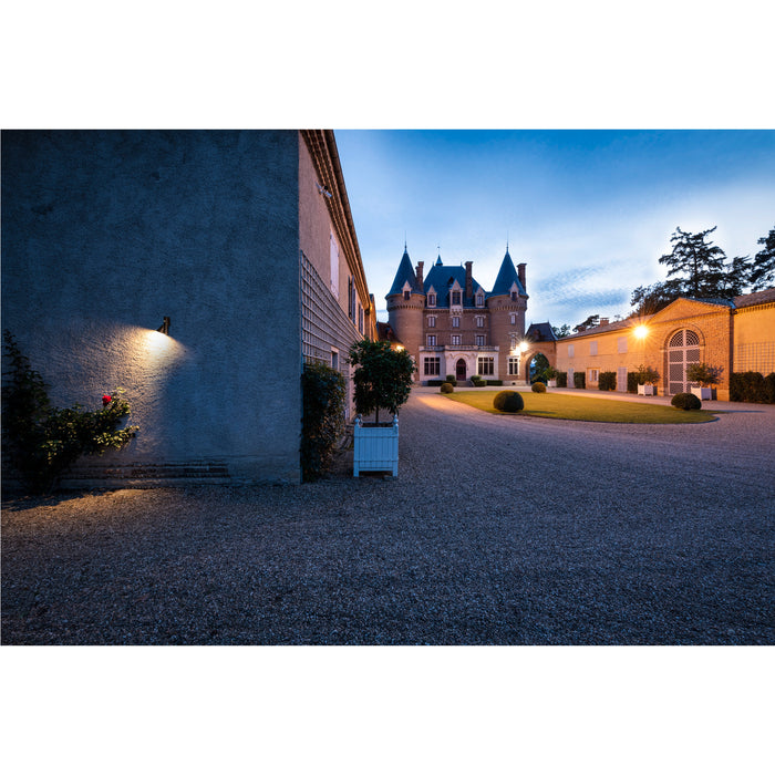 Exterior view of a brick chateau with blue turrets and gravel driveway at dusk.