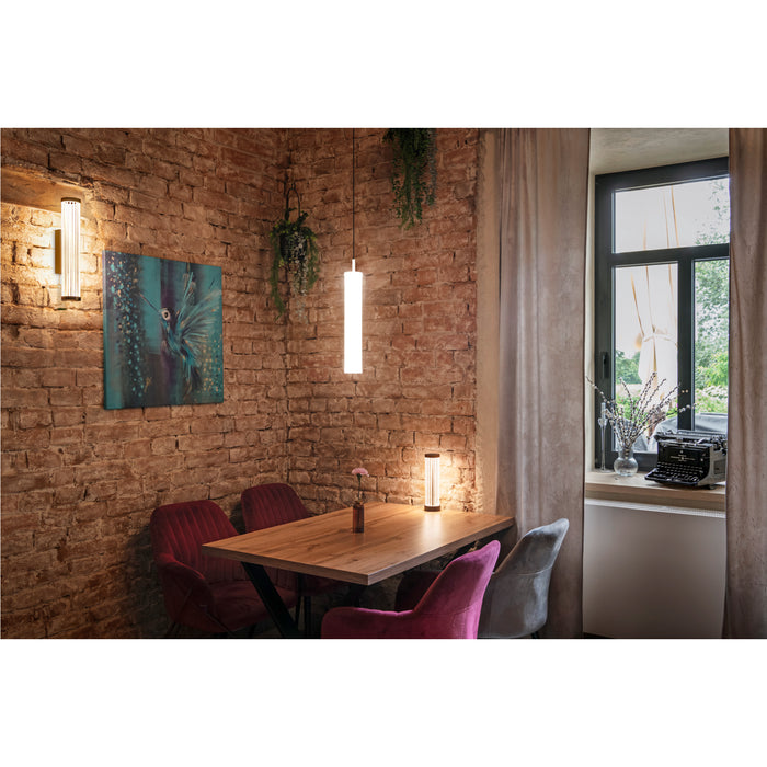 Interior with wood table, red and gray velvet chairs, and cylindrical wall, pendant, and table lamps.