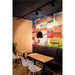 Restaurant interior with black pendant light fixture, wood tables, white chairs, and brown leather booth seating.