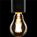 Clear glass light bulb with glowing filament and black textured metal socket.
