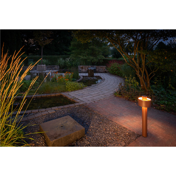 Copper finish bollard light fixture illuminating a garden path.