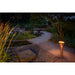 Copper finish bollard light fixture illuminating a garden path.