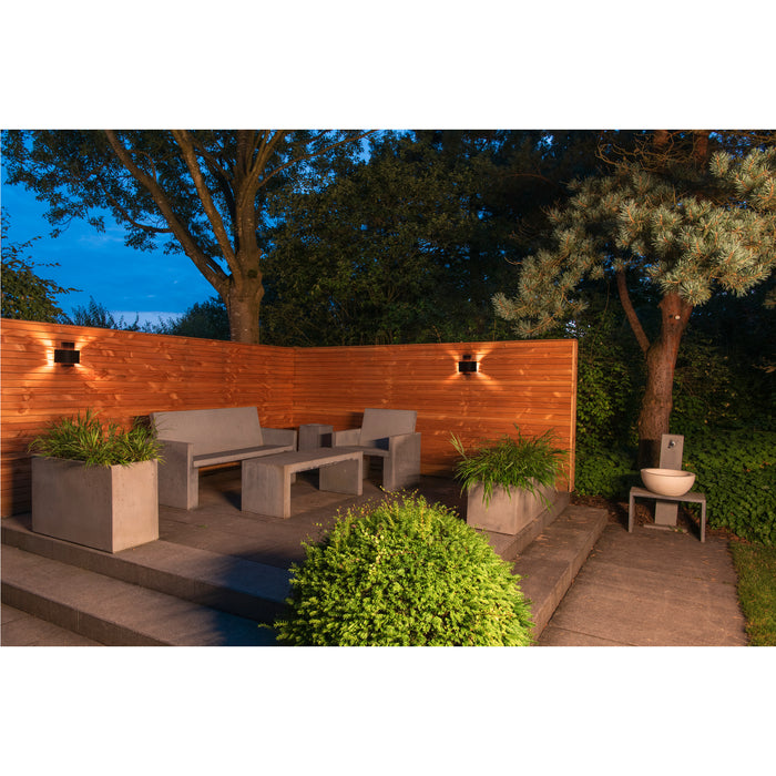 Outdoor patio with concrete furniture, planters, and wall-mounted black lights on a wood fence.