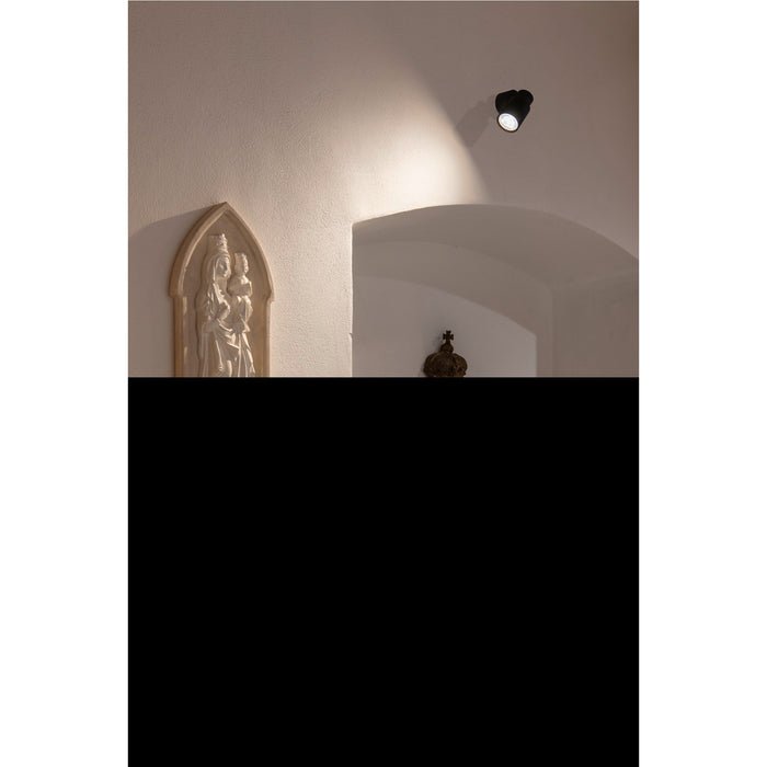 Interior with plaster wall relief of Madonna and Child, black ceiling-mounted spotlight.
