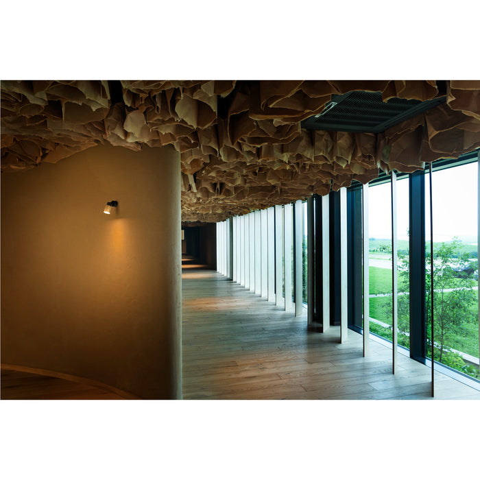 Hallway with wood floor, paper ceiling art, and wall-mounted spotlight.