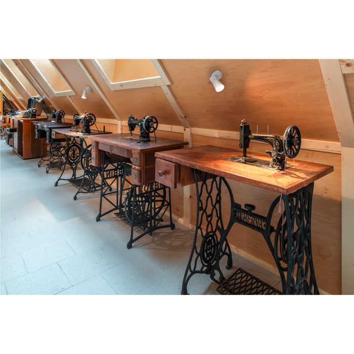 Antique sewing machines with wood tops and ornate black cast iron bases in a bright attic space.