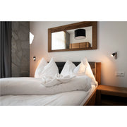 Bedroom with wood bed frame, white linens, and wood-framed mirror.