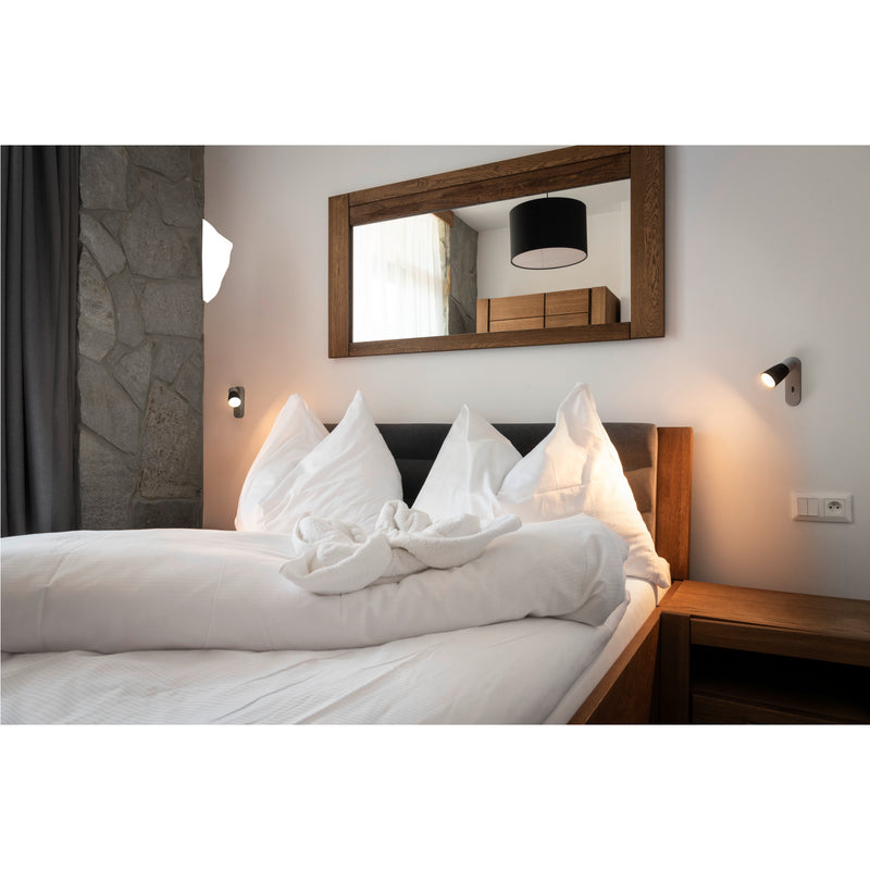 Bedroom with wood bed frame, white linens, and wood-framed mirror.