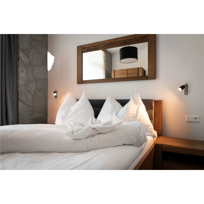 Bedroom with wood bed frame, white linens, and wood-framed mirror.