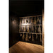 Dried herbs hanging on wooden rods against a dark wall, with a wood floor and a black metal wall-mounted light.