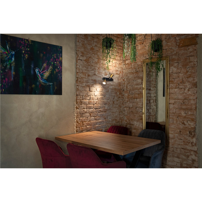 Interior with wood table, velvet chairs, brick wall, gold mirror, and black/gold wall-mounted spotlight.