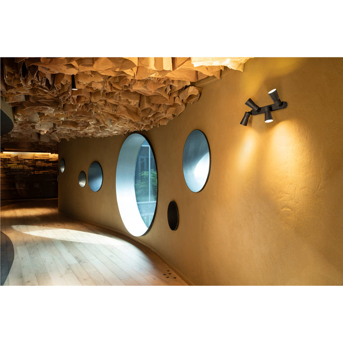 Black metal wall-mounted spotlight with three adjustable heads, illuminating a textured gold wall in a modern interior.