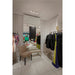 Clothing store fitting room with beige upholstered chair and bench, mirrored wall, and clothing racks.