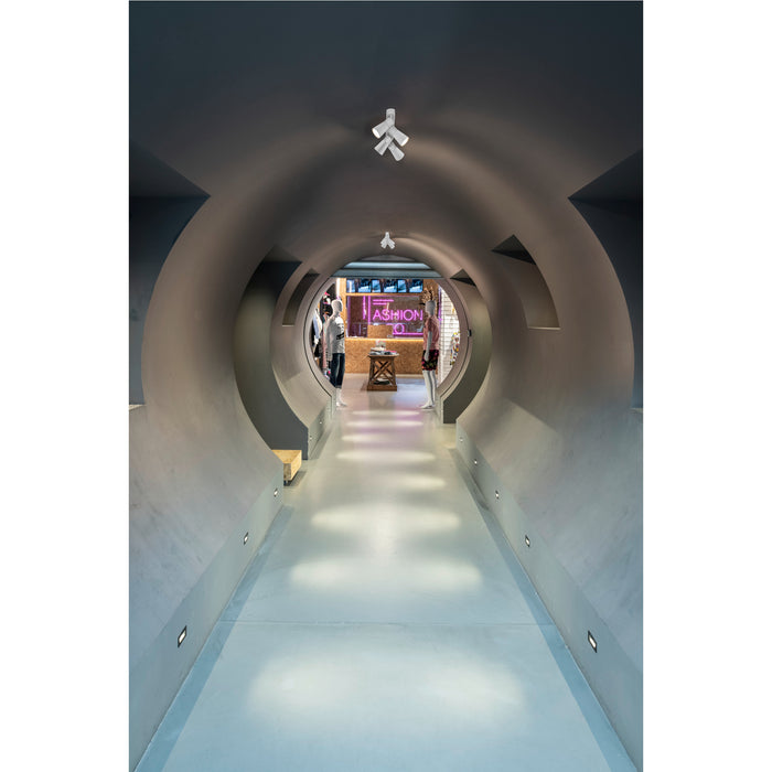 Interior view of a gray concrete tunnel with ceiling-mounted white spotlights leading to a retail space.