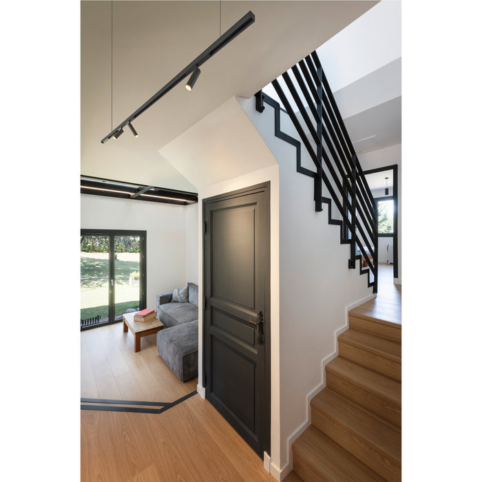 Modern interior with black track lighting, black metal staircase railing, gray door, and light wood stairs.