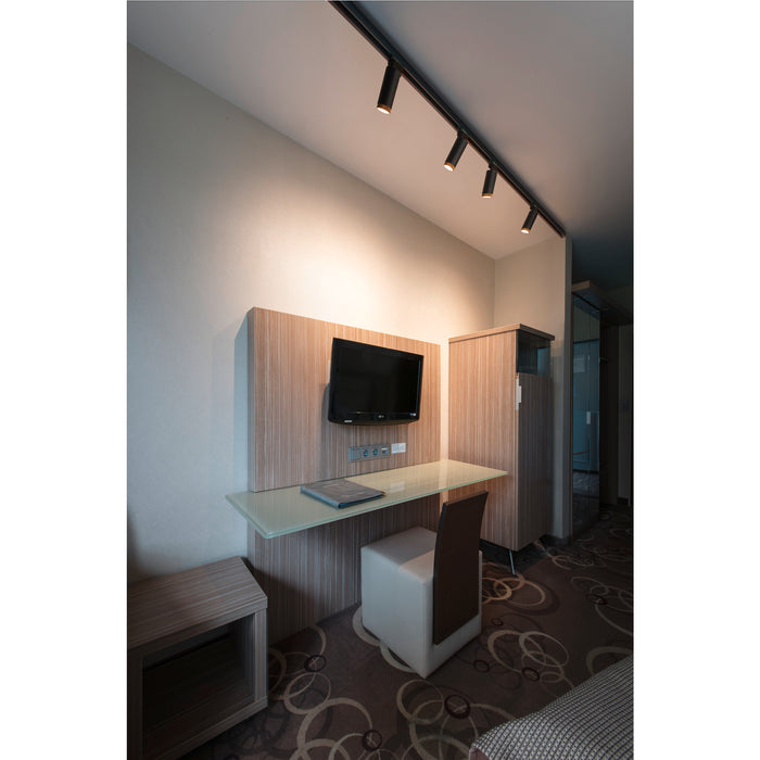 Hotel room interior with wall-mounted TV, glass desk, white leather chair, wood veneer paneling, and black track lighting.
