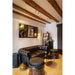 Living room with black leather Chesterfield sofa, metal barrel stools, and track lighting on wood beam ceiling.