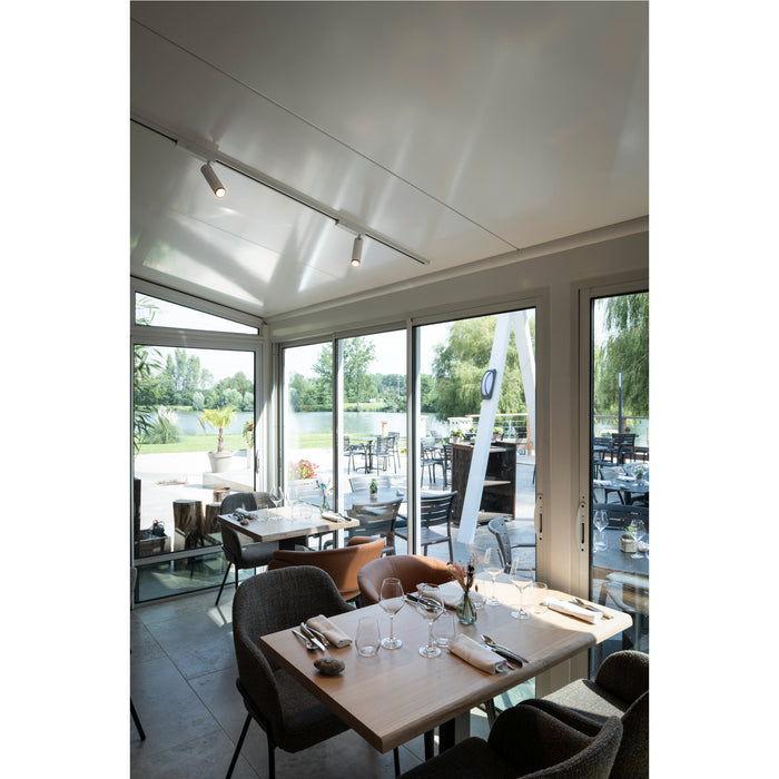 Restaurant interior with tables, chairs, and track lighting; view of outdoor seating and lake.