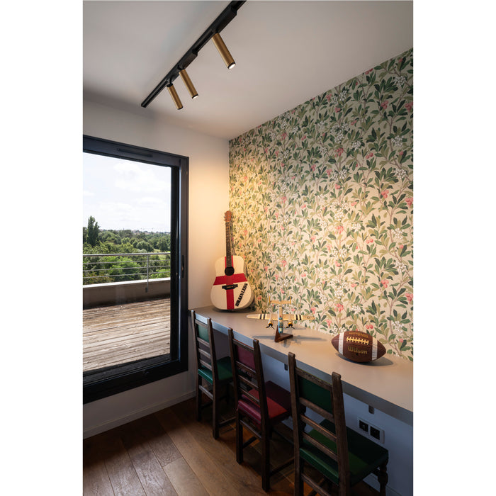 Black track lighting with gold cylinder heads, floral wallpaper, and a desk with chairs in a room with a balcony.